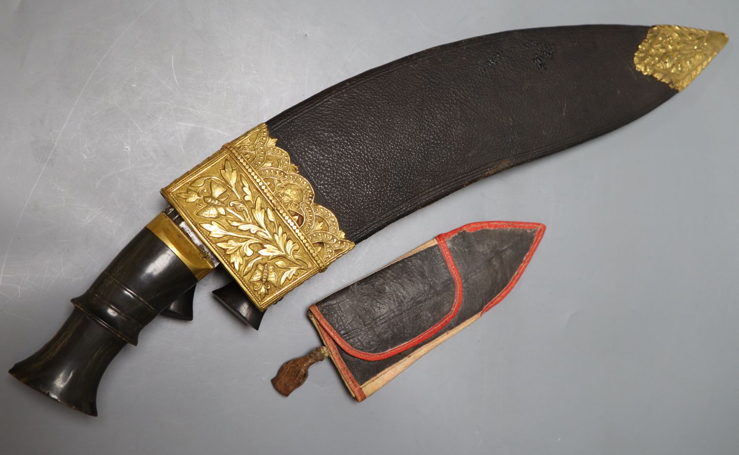 A kukri with skinning knives, leather sheath with elaborate embossed gilt metal mounts, blade 36cm